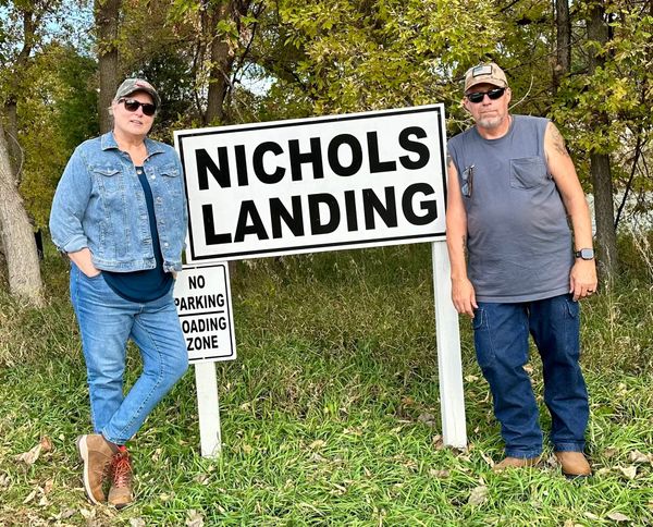 Phil and Lisa standing on either side of a white sign reading “Nichols Landing” near Smith Falls State Park in Nebraska.