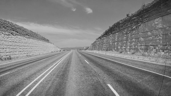 Black-and-white view down an empty highway between tall, layered rock cuts.
