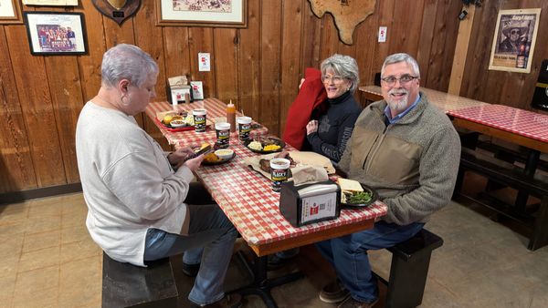 Three diners seated at a checkered table with barbecue and sides inside Black’s Barbecue in Lockhart, Texas.
