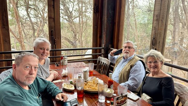 Four diners gathered around a table at the Gristmill, with tall windows overlooking trees.