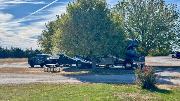 Large Super C motorhome and pickup truck parked at a spacious campsite beneath mature trees at Fishberry Campground near Valentine, Nebraska.