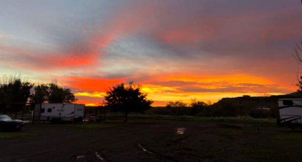 Orange and pink sunset over McMillan RV Park in Fort Davis, Texas, with RVs and trees silhouetted in the foreground.
