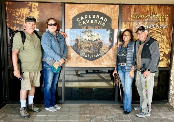 Four visitors standing outside the Carlsbad Caverns National Park visitor center beside a centennial display marking 1923–2023.