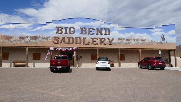 Big Bend Saddlery storefront in Alpine, Texas, with a cattle mural above the covered entrance.