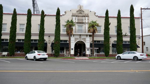 Hotel Paisano’s white facade in Marfa, Texas, with an ornate entrance, tall narrow trees and palm trees.
