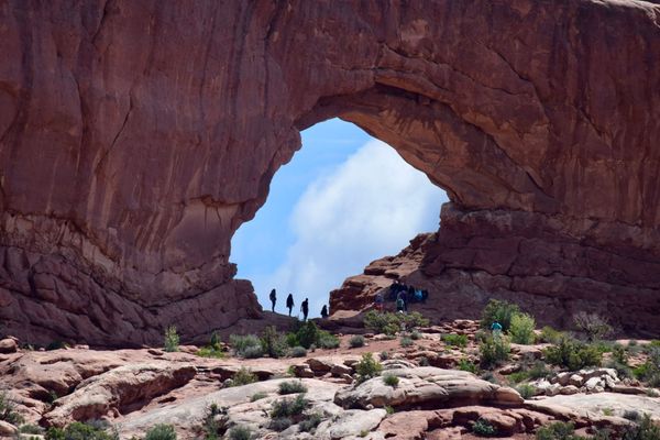 Visitors walking beneath a large red sandstone arch at Arches National Park near Moab, Utah.