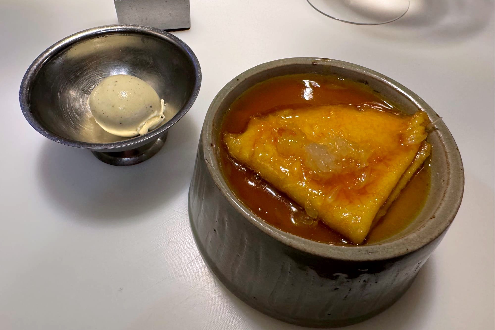 Folded crêpe in citrusy yuzu-orange sauce beside a scoop of vanilla ice cream.