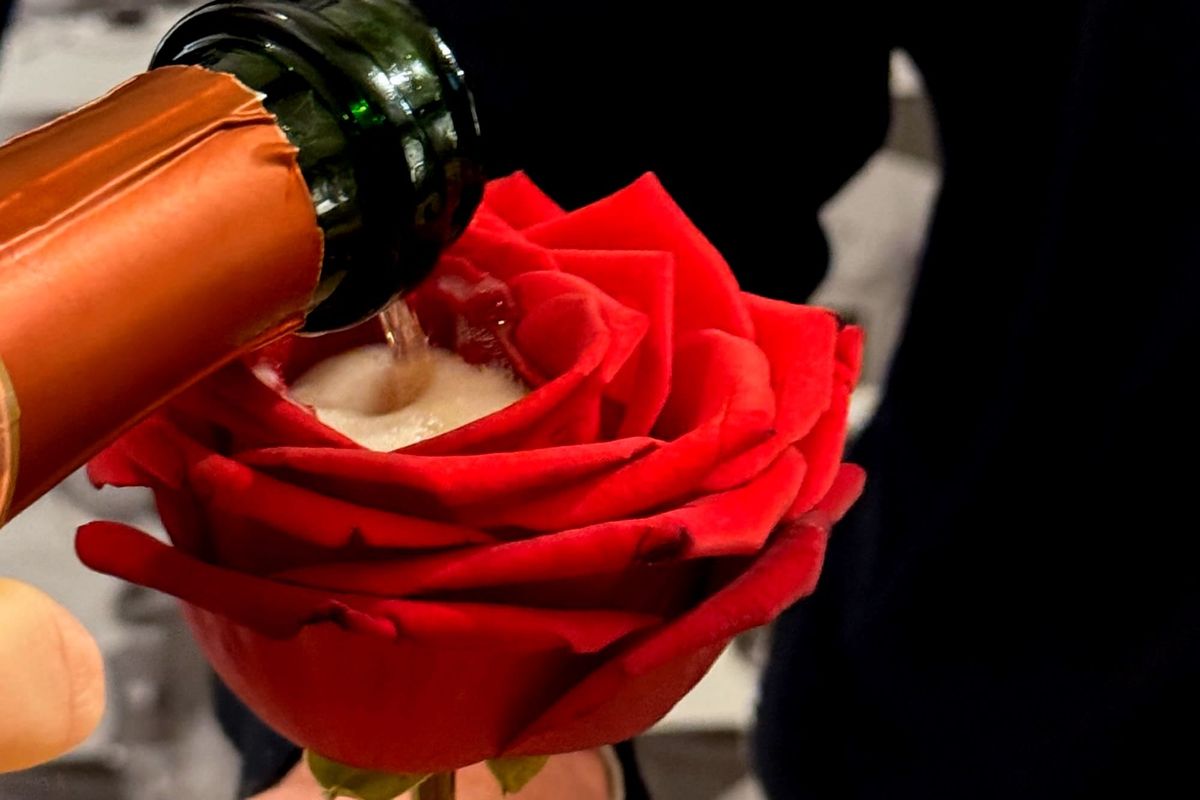 Laurent-Perrier champagne being poured into a fresh red rose held by a server, with the champagne filling the petals as part of a fine dining presentation.