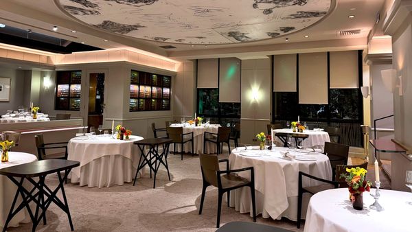 Elegant dining room at Restaurant Pierre Gagnaire in Paris, with round tables, white tablecloths and the signature illustrated ceiling.