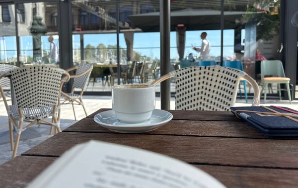 A book, slightly out of focus, with a coffee cup in the background, in focus.