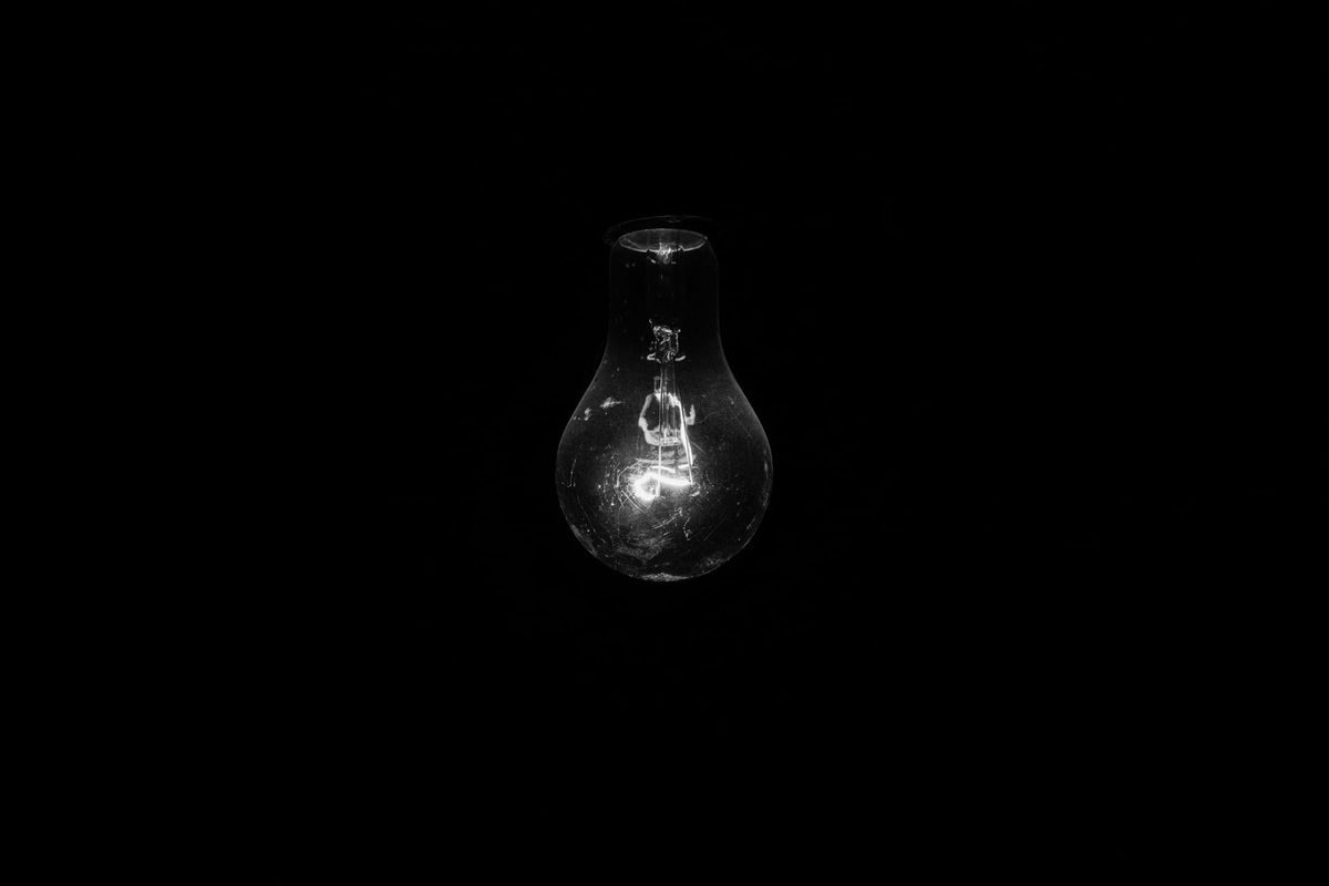 A single illuminated light bulb glowing, emphasizing its form and intricate filament, against a completely black background.
