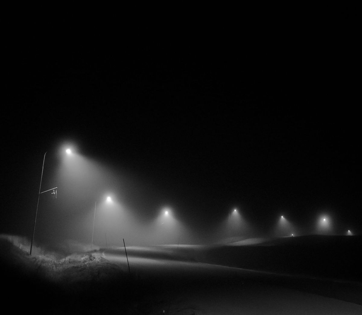 A foggy road at night with a row of glowing streetlights receding into the distance.