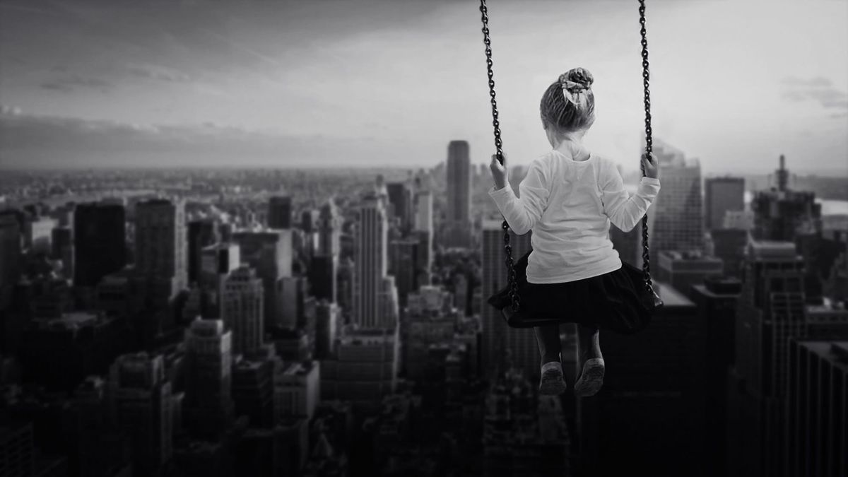 Black-and-white image of a woman on a swing, seen from behind, overlooking a dense city skyline; the scene feels quiet and contemplative.
