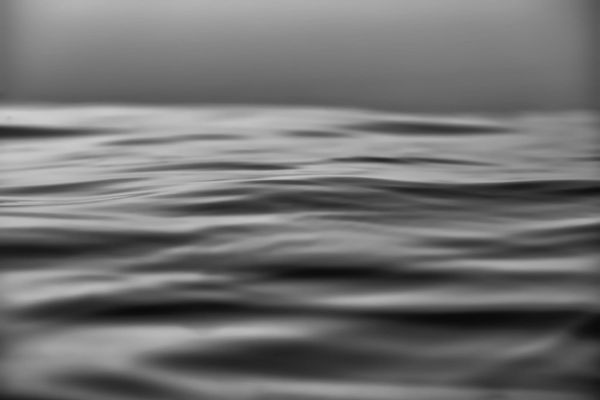 Blurred grayscale image of a serene ocean surface with gentle ripples, evoking a calm and peaceful atmosphere under an overcast sky.