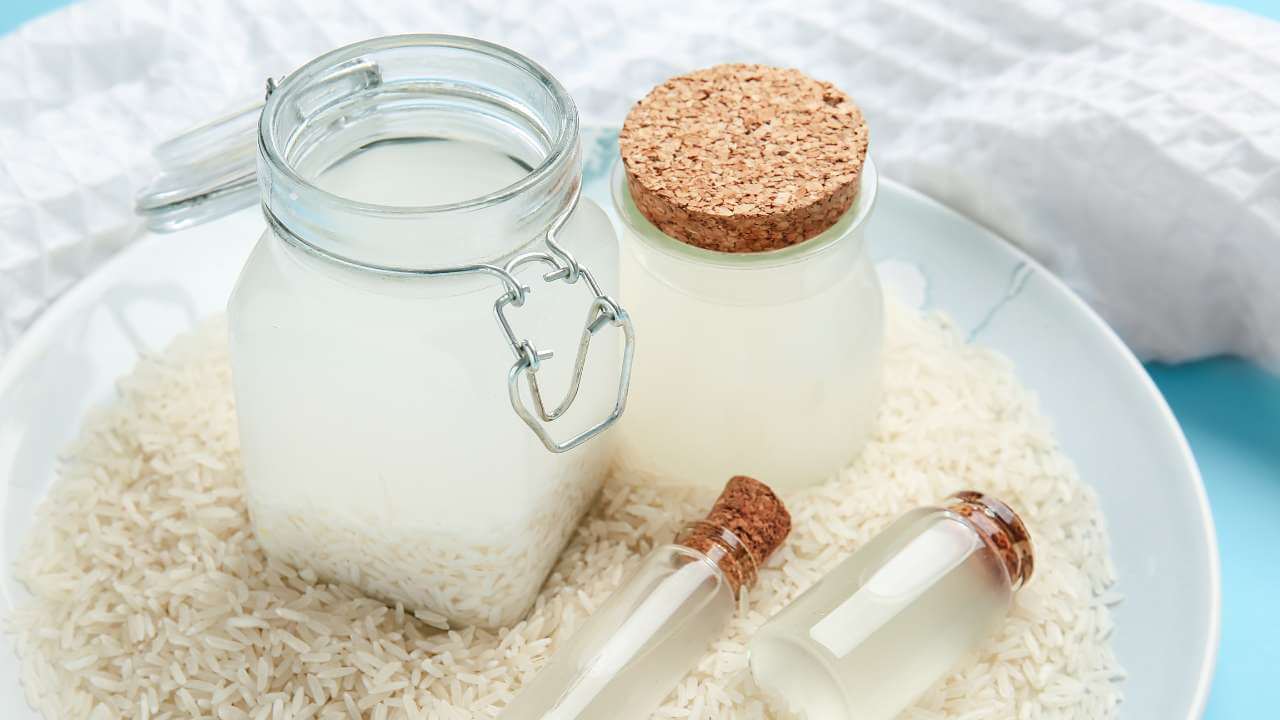 1 large mason jar, 1 medium jar, and 2 small glass jars filled with fermented rice water on a white plate covered in rice. 