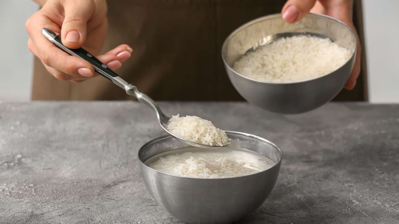 Woman begins to prepare rice water in a stainless-steel bowl on top of gray counter after boiling rice in plain water.