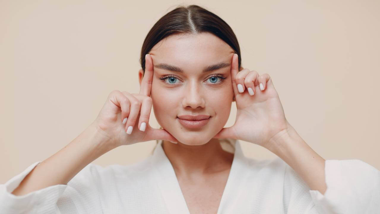 Woman lifts her eyebrows with both hands to reduce wrinkles and visible signs of fine lines while making facial expressions.