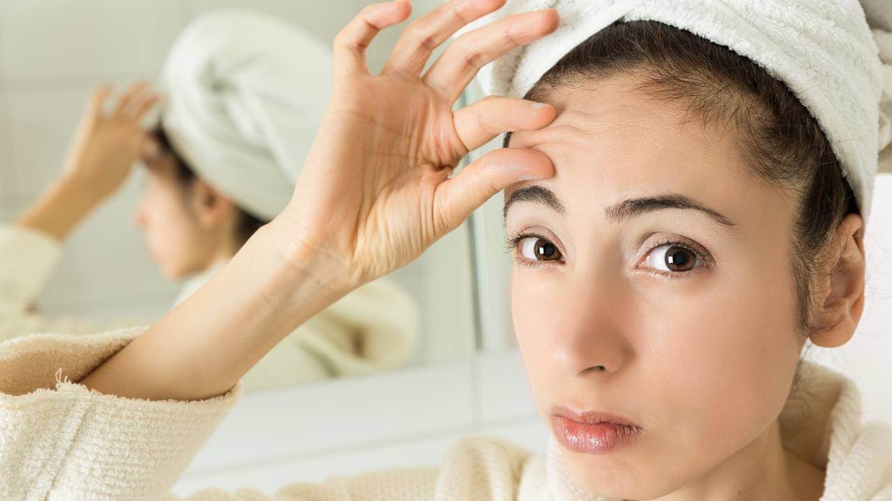 A woman concerned with visible signs of early lines and wrinkles on her forehead above her eyebrows.