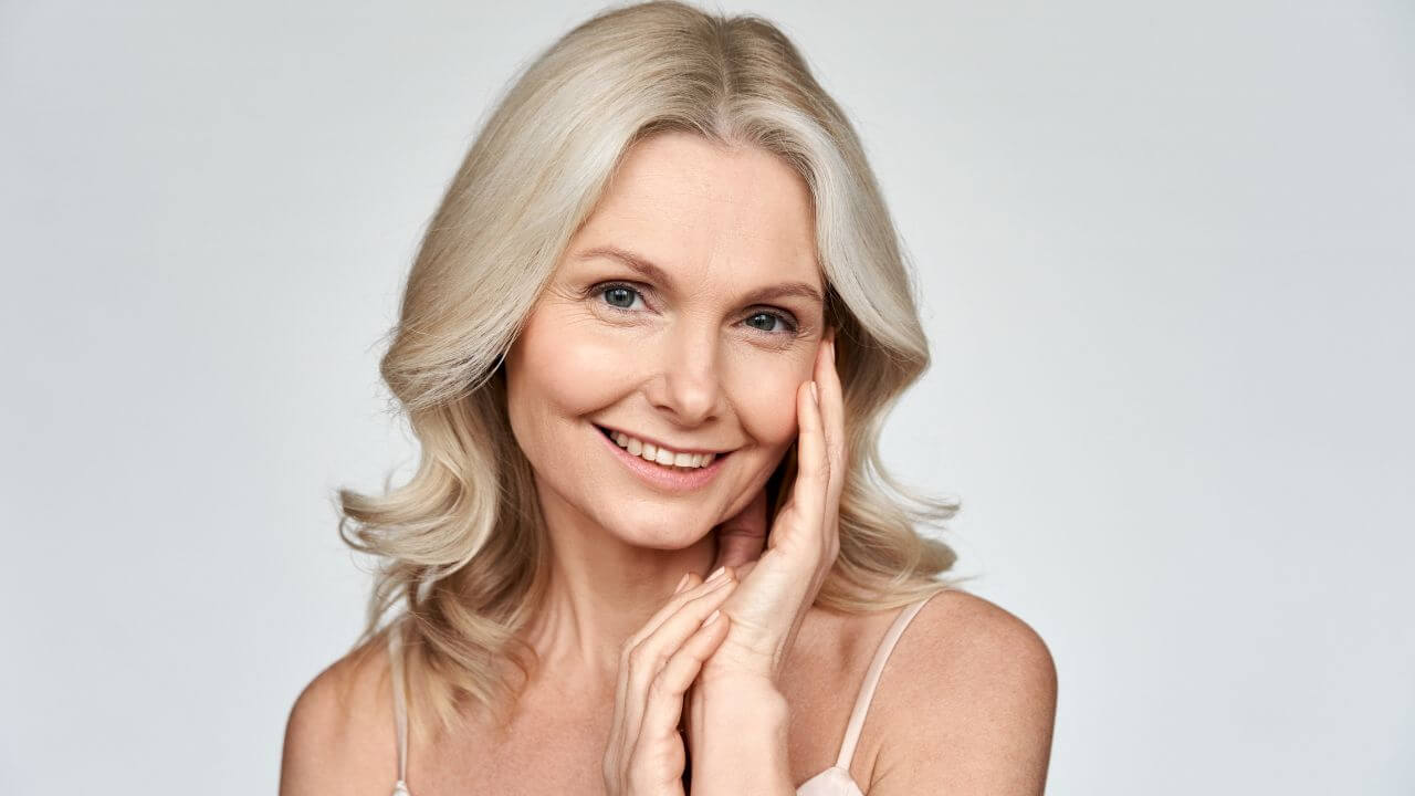 Smiling older woman touching her face with a youthful glow since using collagen supplements for younger looking skin.