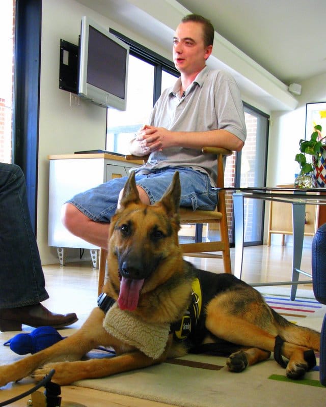 Joe Stalnaker seated at home with Buddy, his German shepherd assistance dog, lying in the foreground.