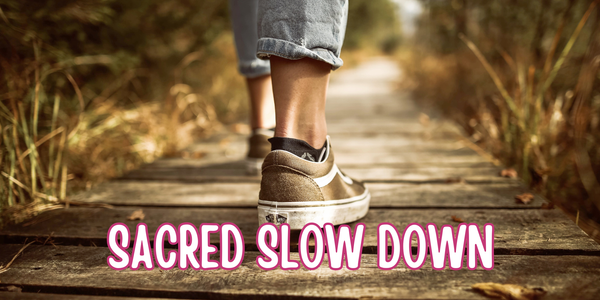 Two legs in tan suede Vans walking on a wooden path, flanked by grassy reeds. The path fades into the distance.