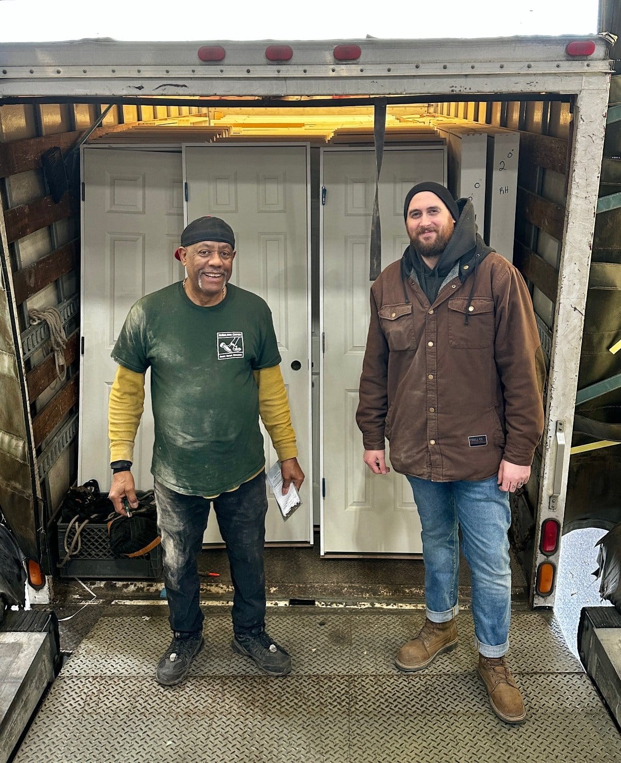 two men at the back of a truck full of doors smoking at the camera