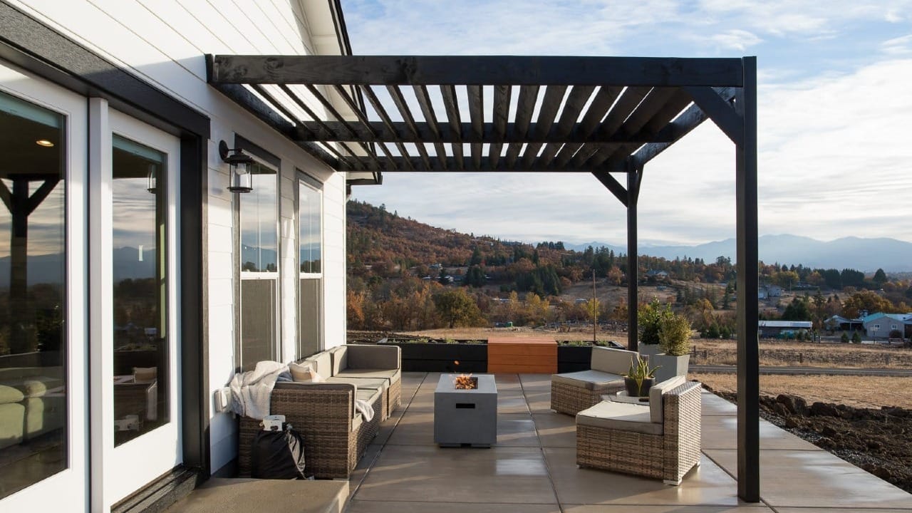 Custom home covered patio with pergola, outdoor seating, fire feature, and scenic hillside views beyond the property.