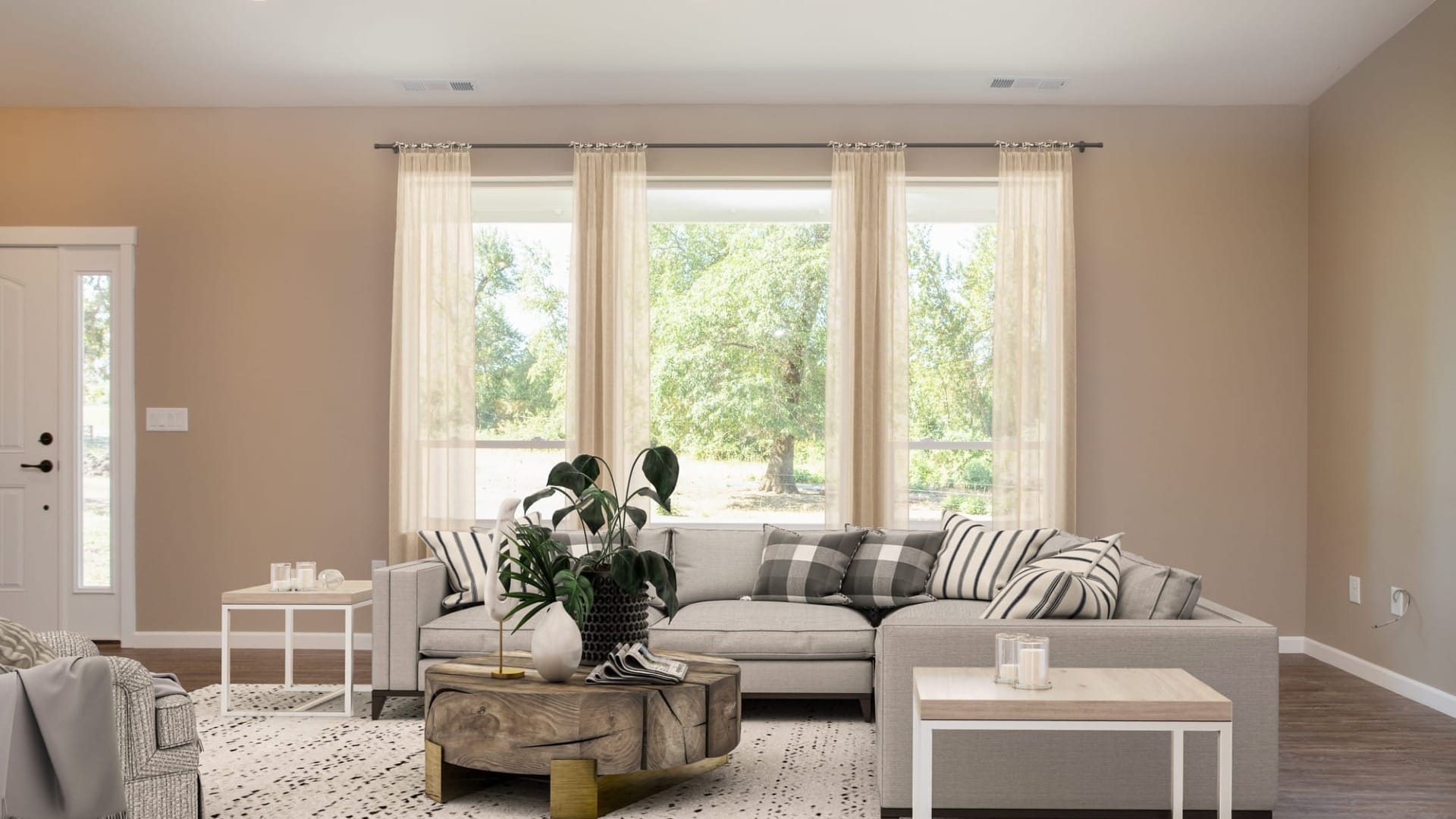 A bright living room with large windows, neutral beige walls, a light gray sectional sofa, striped pillows, and a wood block coffee table.