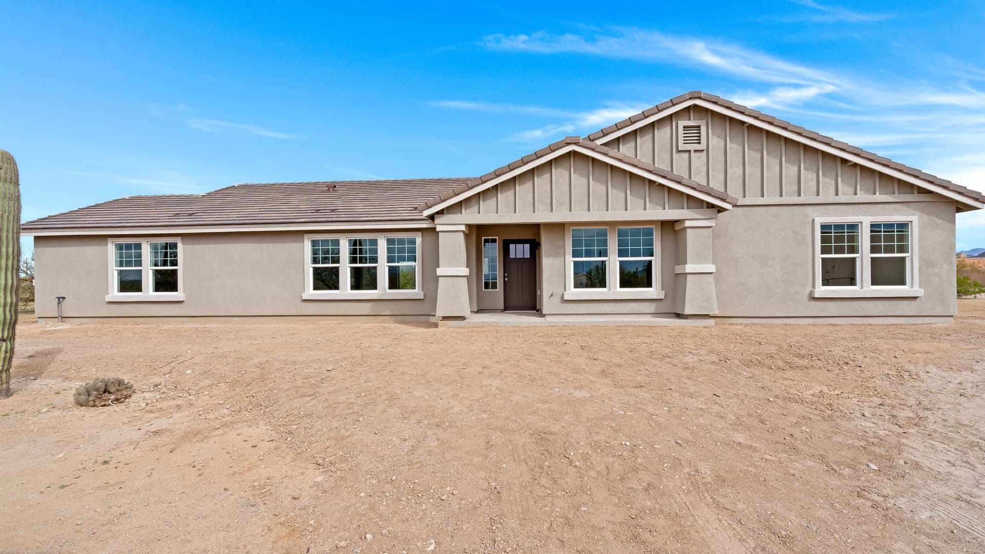 Single story custom home with craftsman style details, gabled rooflines, covered porch, and simple desert surroundings.