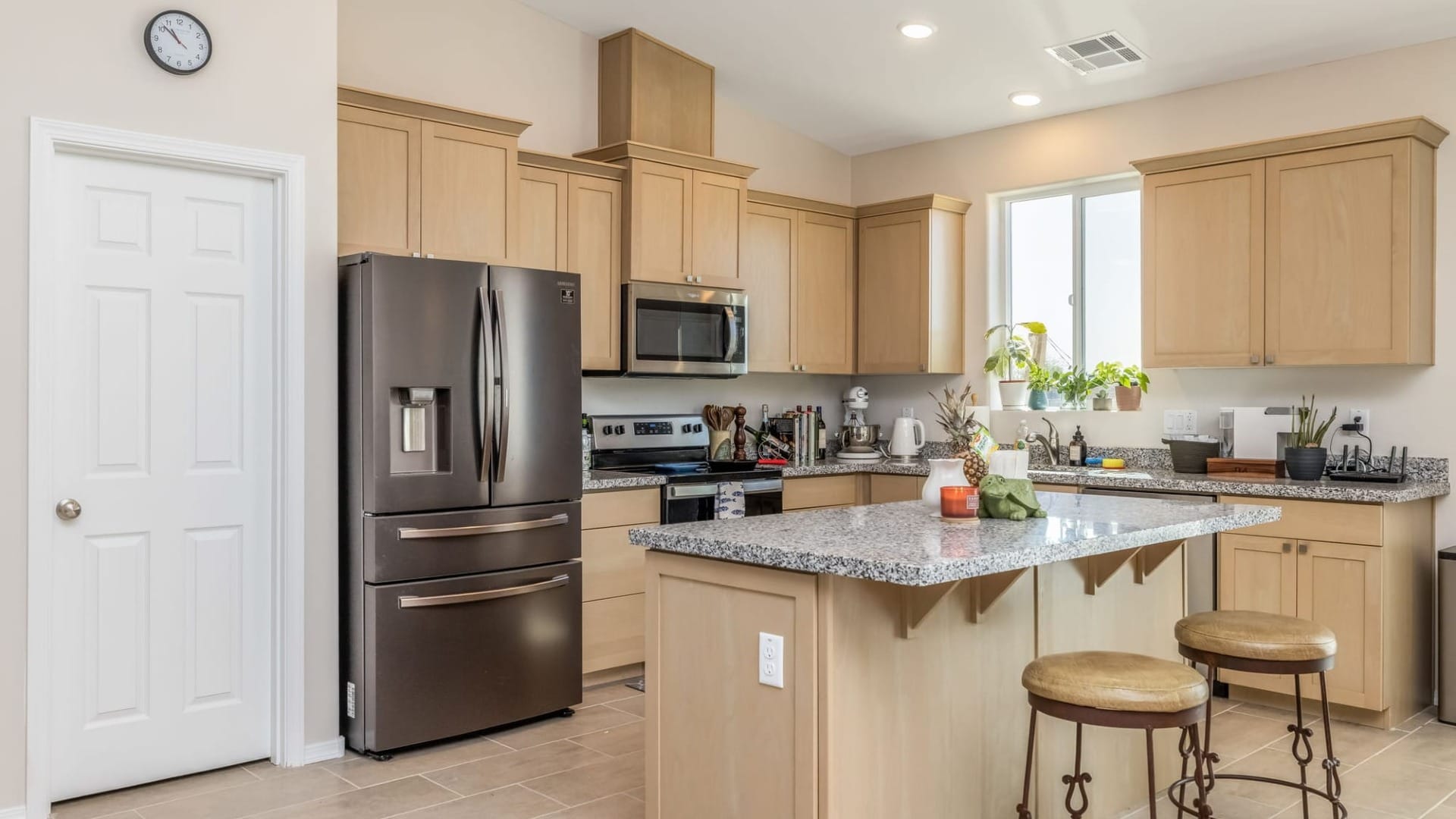 Custom home kitchen featuring light wood cabinetry, granite island, stainless steel appliances, and seating at the center island.