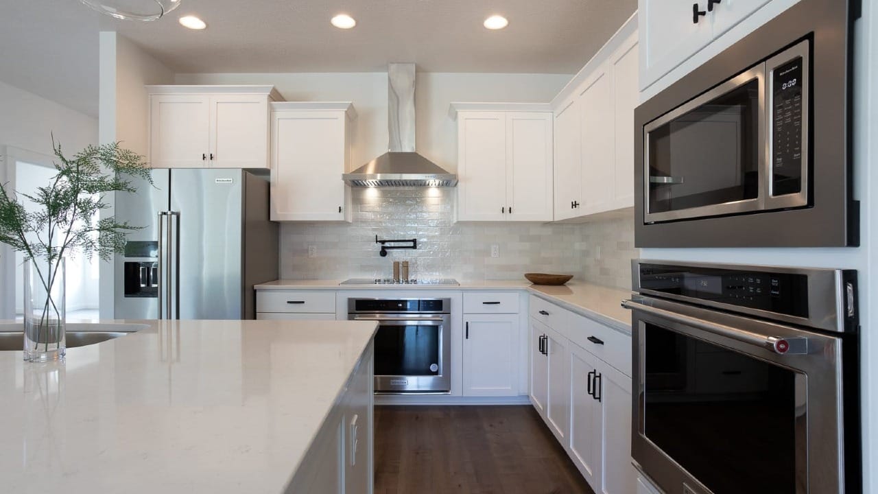Custom home kitchen with white cabinetry, quartz countertops, stainless steel appliances, built in oven, and large center island.