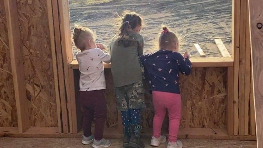 Three children looking outside of a window frame