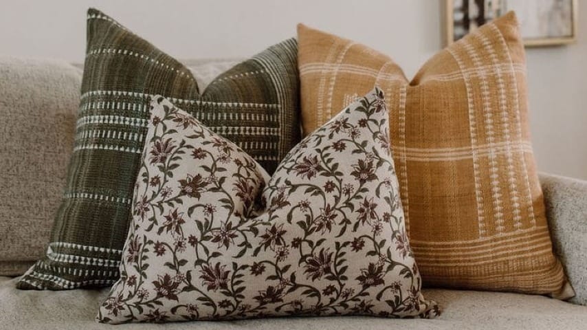 Three pillows that are fall themed on a couch