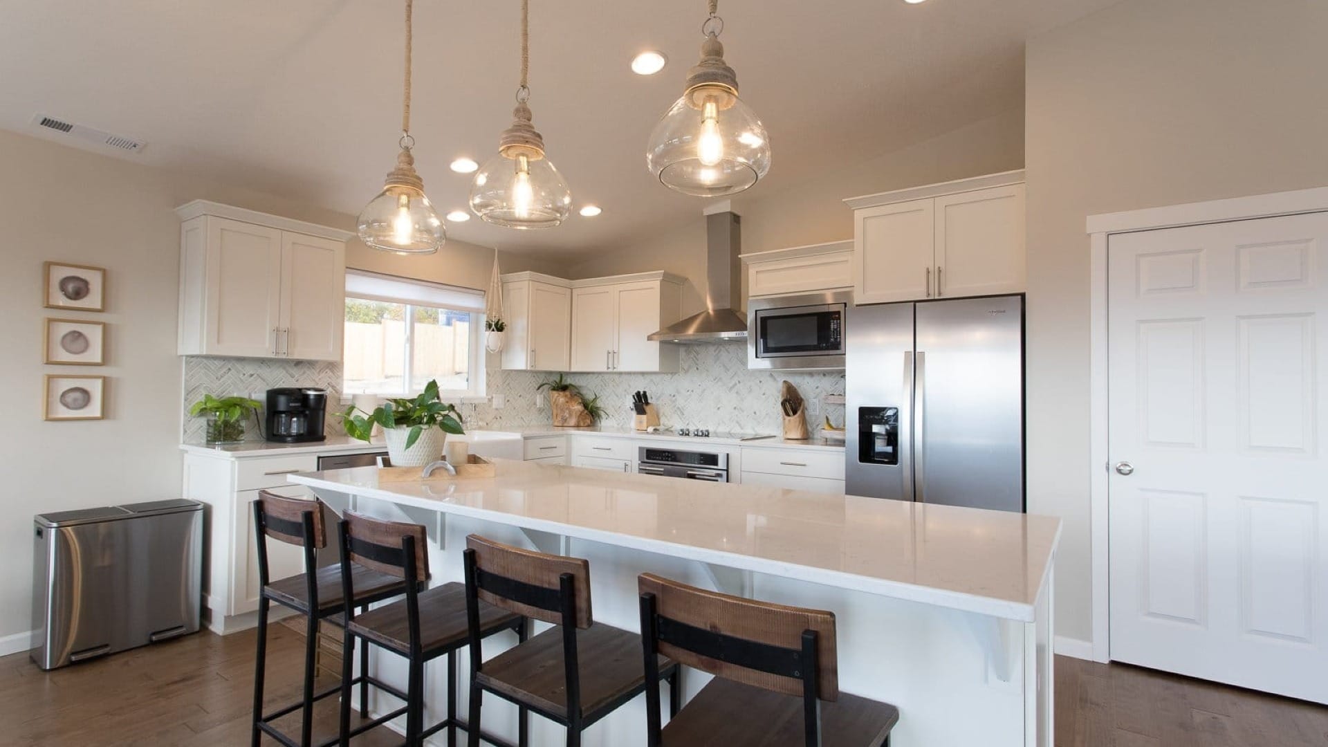 Custom home kitchen with white cabinets, large island, pendant lighting, stainless steel appliances, and clean modern design.