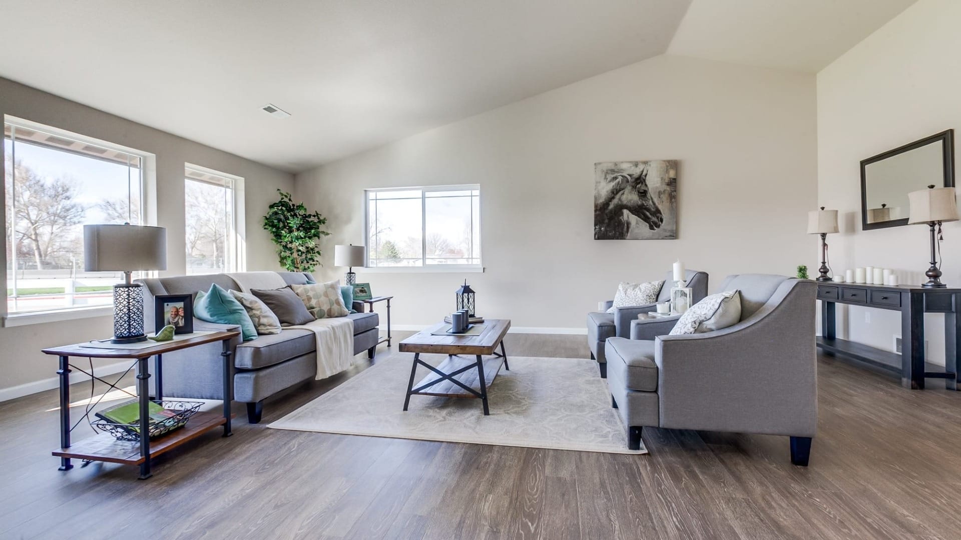 A bright living room with neutral furniture, large windows, indoor plants, and a horse painting accenting the wall.