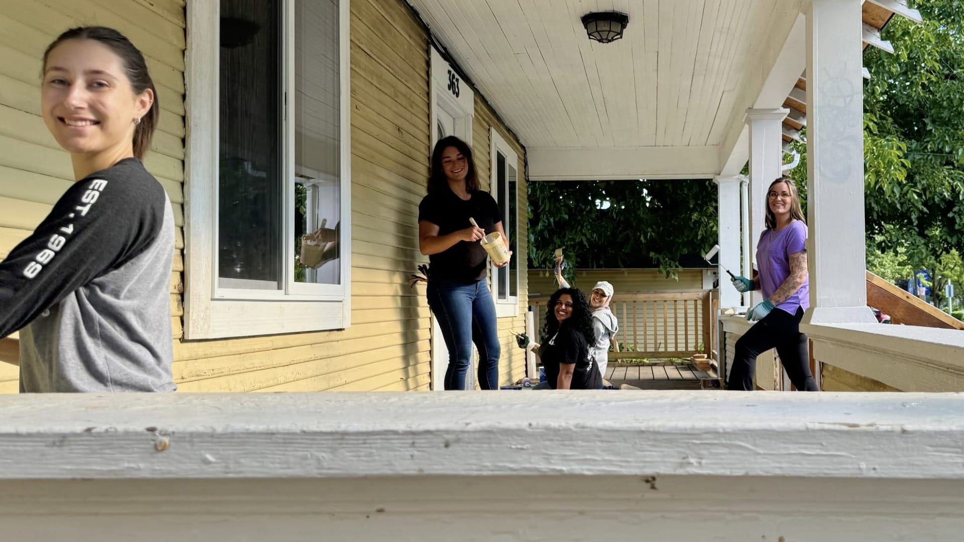 women painting outside of yellow house