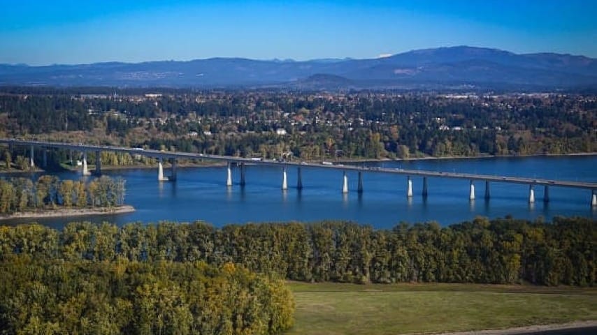 Scenic aerial view of a wide river with a long bridge crossing through forested land and nearby communities.