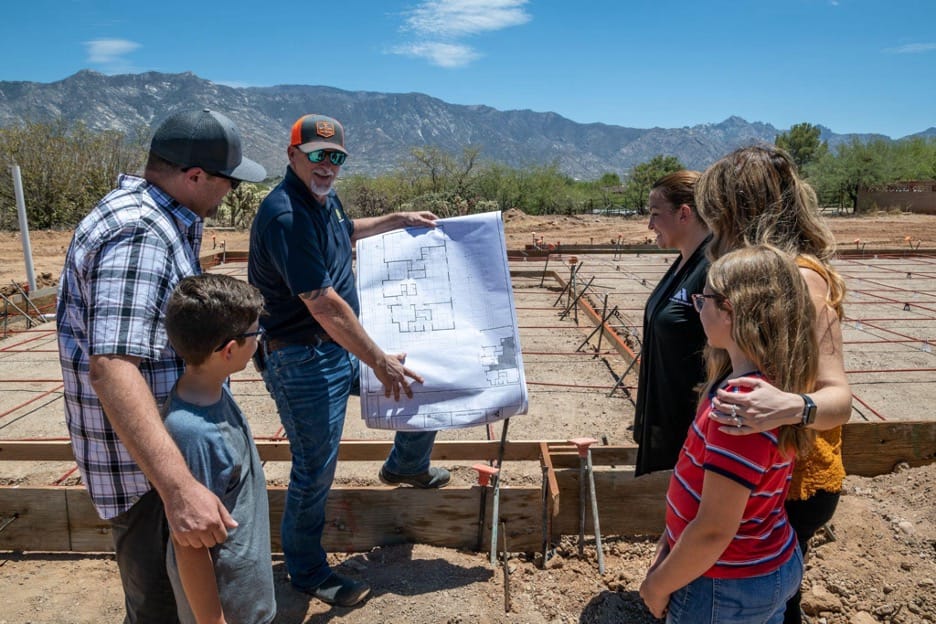 family of four looking at blue prints that contractors from Adair homes have created for their home