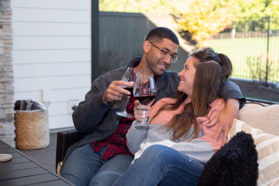 husband and wife sitting outside on a couch drinking Wine and smiling at each other