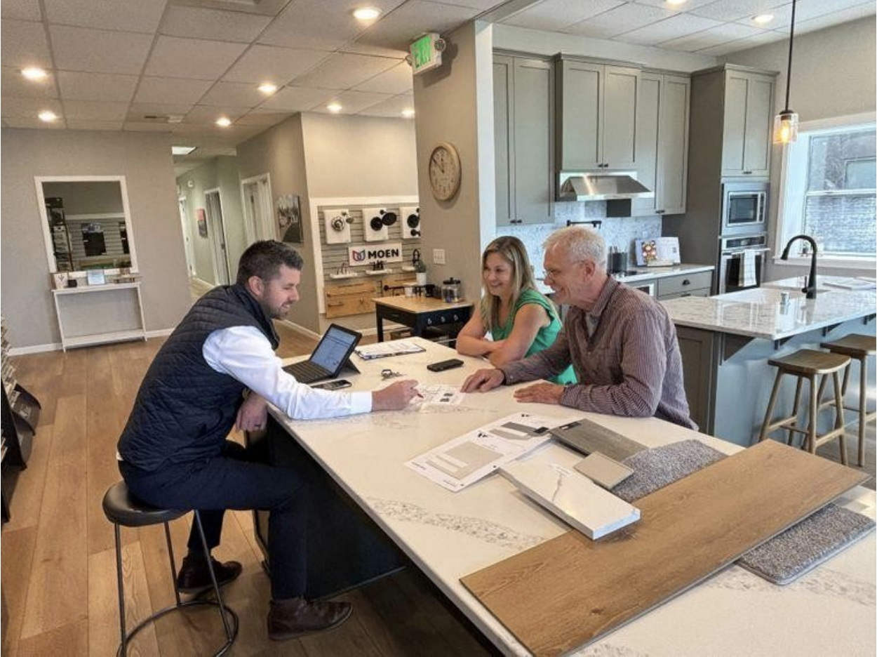 Two people meeting with a consultant at a design center table, reviewing home plans and material samples.