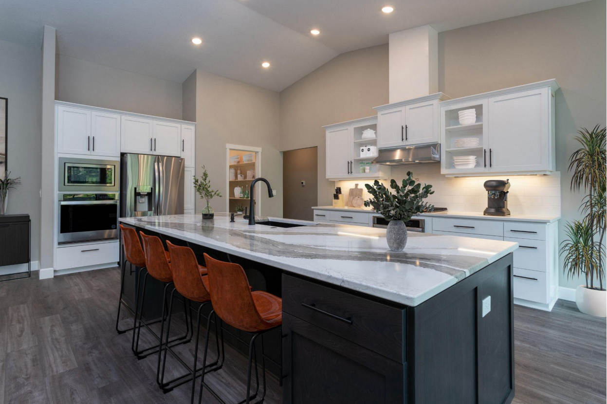 A modern kitchen with a large marble island, white cabinetry, stainless steel appliances, and barstool seating.