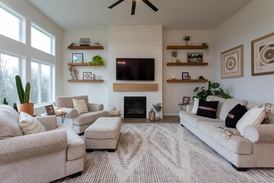 A modern living room with large windows, neutral furniture, a shiplap fireplace, floating wood shelves, and warm natural décor.