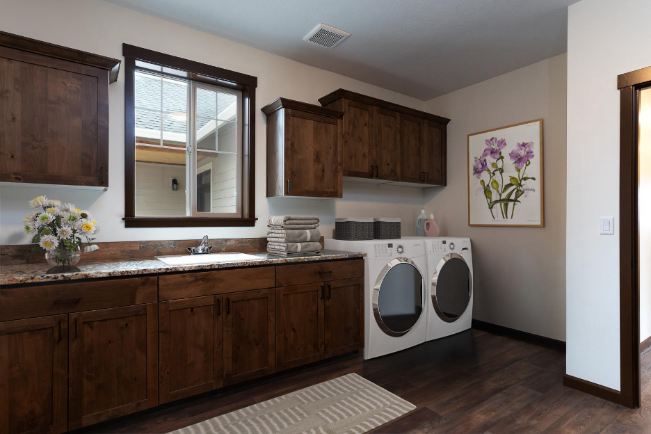 Spacious laundry room with rich wood cabinetry, granite countertops, front-loading washer and dryer, and a window providing natural light.