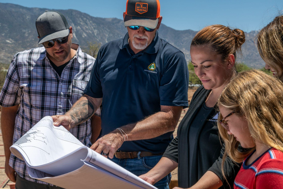 Adair Homes team reviewing blueprints with a family on-site against a scenic mountain backdrop.