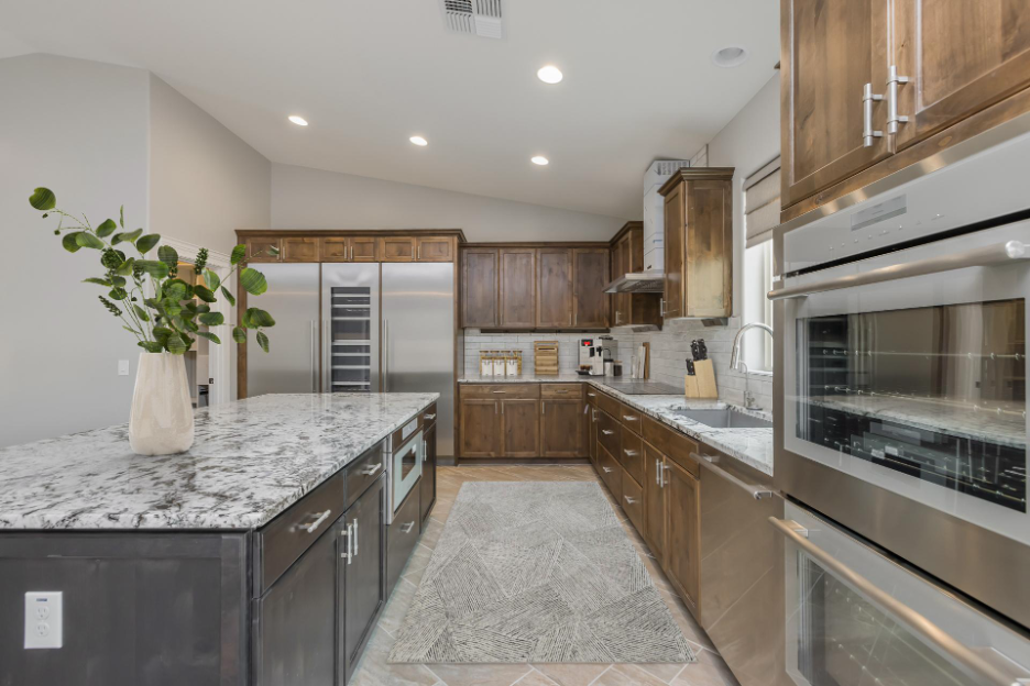Contemporary kitchen featuring rich wood cabinetry, marble countertops, stainless steel appliances, and a large island with modern lighting and sleek finishes.