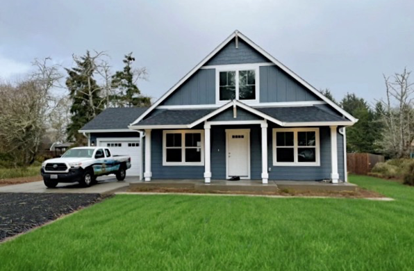 Charming craftsman-style home with front porch, gable roof, and navy blue siding—Adair Homes construction vehicle parked in the driveway.