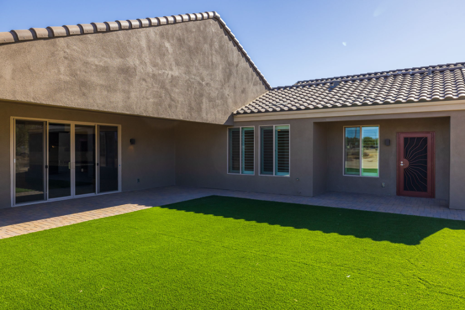 Modern stucco home exterior with tile roofing, large sliding glass doors, and a private courtyard featuring artificial turf and a brick patio walkway.