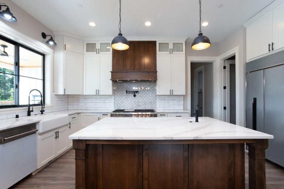 Modern farmhouse kitchen featuring a large marble island, wood cabinetry, white shaker cabinets, subway tile backsplash, and black pendant lighting.