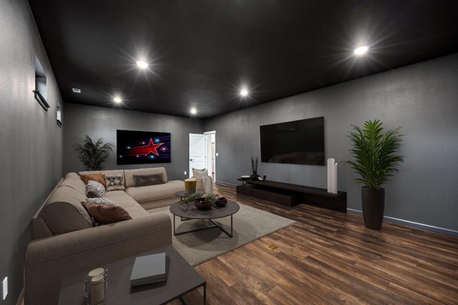 Modern home theater room featuring a large sectional sofa, dark gray walls, wood flooring, recessed lighting, and dual flat-screen TVs with minimal décor.