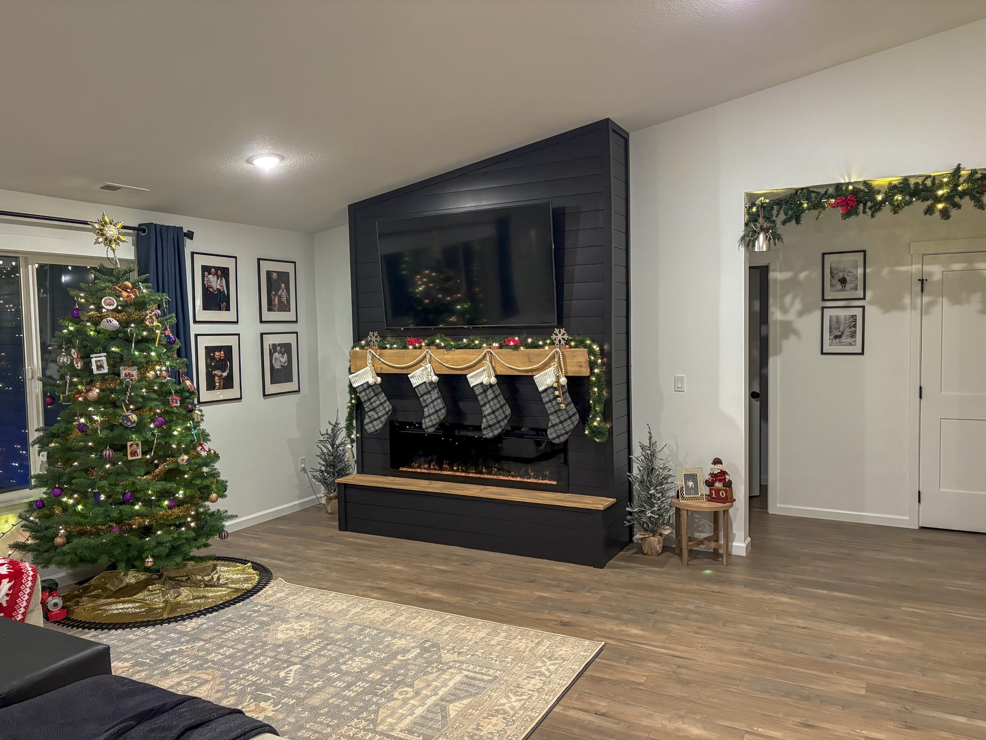 Modern living room with a Christmas tree and a dark shiplap fireplace decorated with stockings and garland.